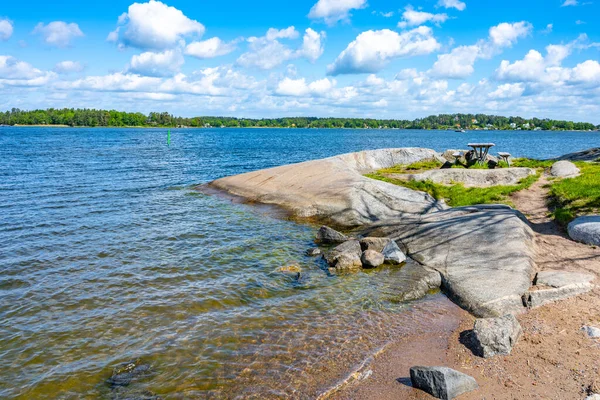 Small beach with flat stones, a bench, and an amazing view of other islands on a sunny summer day. Island of Vaxholm, Stockholm Archipelago, Sweden