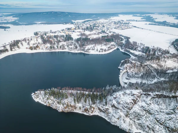 Sec water reservoir with concrete dam and wintertime snowy hills of Iron Mountains around. Czechia. Aerial view from drone.