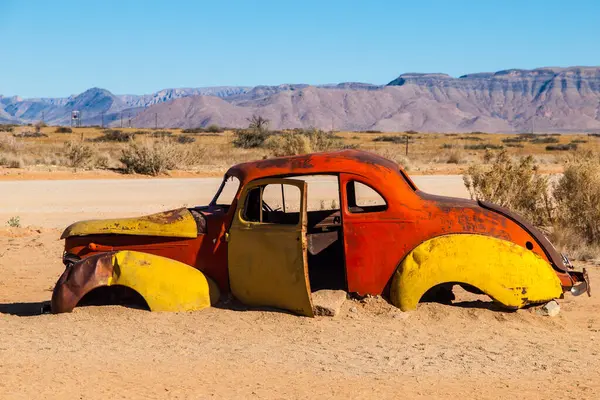 Rustic, weather-beaten cars lie abandoned amidst the stark landscape of Solitaire in Namibia, their vibrant colors contrasting with the arid desert backdrop.