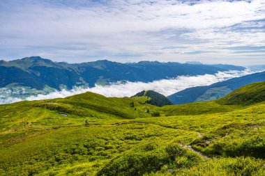 A hiker explores the lush trails of the Austrian Alps with a majestic mountainous backdrop and low-hanging clouds. Salzach Valley, Hohe Tauern, Austria clipart