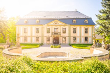 Photo of Potstejn, a charming baroque chateau in Czechia. Yellow facade, dark blue roof, surrounded by lush greenery, trees, and a garden. clipart