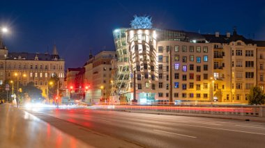 The Dancing House in Prague is illuminated by the city lights at dusk. The unique deconstructivist architecture stands out against the backdrop of traditional buildings. Light trails from passing cars clipart