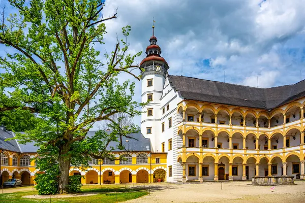 stock image Serene courtyard of Velke Losiny Chateau, surrounded by beautiful architecture and a majestic tree under a partly cloudy sky, showcasing the charm of Czechias rich history.