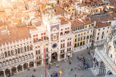 The majestic St Marks Clocktower stands prominently at sunset, surrounded by bustling crowds in the historic Piazza San Marco in Venice, Italy. Architectural beauty and lively atmosphere combine. clipart