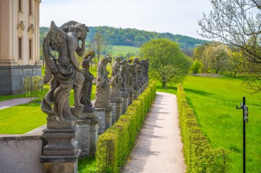 Baroque statues elegantly decorate the pathway at the Kuks hospital complex in Czechia, surrounded by lush greenery and hills under a clear sky. clipart