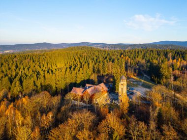 A sunny autumn morning reveals the Bramberk lookout tower and hut nestled in the Jizera Mountains, surrounded by vibrant foliage and serene landscapes. clipart