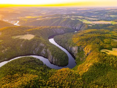 A breathtaking sunset bathes the Vltava River in golden hues, casting reflections on its winding path. Surrounded by lush hills and valleys, this serene moment captures the natural beauty of Czechia. clipart