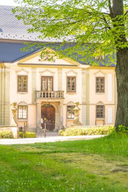 A sunny view of the small Baroque chateau Potstejn in Czechia, with its yellow facade and green trees. clipart