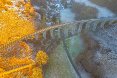 A beautiful winter sunset casts golden hues over the railway stone bridge in Novina, Krystofovo udoli. The surrounding landscape features a serene atmosphere with frost-covered fields. clipart