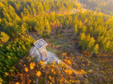 The Cisarsky Kamen wooden lookout tower stands majestically amidst vibrant autumn foliage, offering stunning views as the sun sets over the tranquil landscape near Liberec. clipart