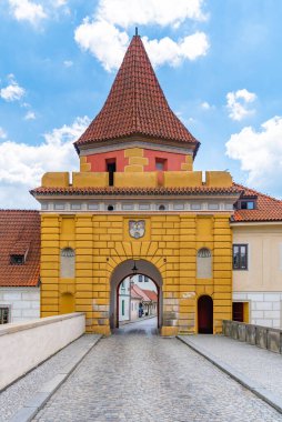 The vibrant yellow Budejovicka Gate stands majestically under a blue sky, inviting visitors to explore the historic streets of Cesky Krumlov. clipart