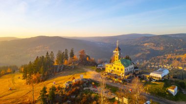 The Tanvaldsky Spicak lookout tower stands majestically in the Jizera Mountains, bathed in the warm glow of an autumn evening, surrounded by colorful foliage and rolling hills. clipart