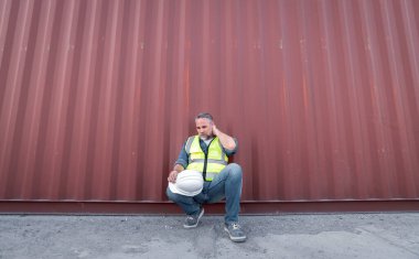 Mühendis ya da işçi kargo konteynırına yakın otururlar. İş yerinde uzun süre çalıştıktan sonra yorgun görünürler. İşle ilgili ciddi görünürler..