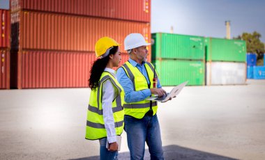 Engineers wearing safe uniform with radio communication working in the construction container dock yard checking and inspection containers data is container shipping Logistics business concept.