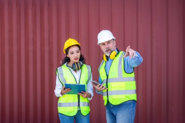 Engineers wearing safe uniform with radio communication working in the construction container dock yard checking and inspection containers data is container shipping Logistics business concept.