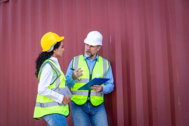 Engineers wearing safe uniform with radio communication working in the construction container dock yard checking and inspection containers data is container shipping Logistics business concept.