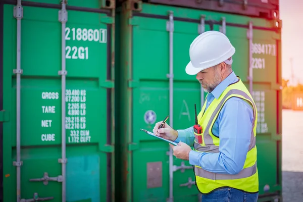 Engineers wearing safe uniform with radio communication working in the construction container dock yard checking and inspection containers data is container shipping Logistics business concept.