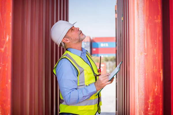 Engineers wearing safe uniform with radio communication working in the construction container dock yard checking and inspection containers data is container shipping Logistics business concept.