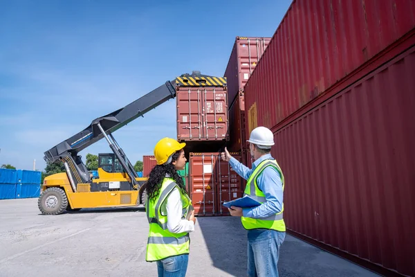 Engineers wearing safe uniform with radio communication working in the construction container dock yard checking and inspection containers data is container shipping Logistics business concept.