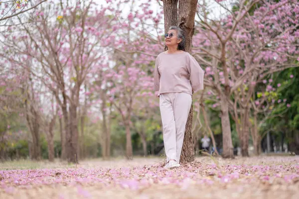 Gri saçlı yaşlı kadınlar birlikte güzel bir anın tadını çıkarıyorlar. Etrafı çiçek açan pembe çiçeklerle çevrili. İfadeler derin dostluk ve mutluluğu yansıtıyor..