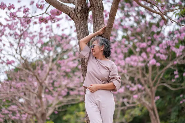 Gri saçlı yaşlı kadınlar birlikte güzel bir anın tadını çıkarıyorlar. Etrafı çiçek açan pembe çiçeklerle çevrili. İfadeler derin dostluk ve mutluluğu yansıtıyor..