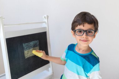 Gözlüklü sevimli çocuk tahtaya Ukrayna bayrağı çiziyor. Tebeşirle. Anaokulu öğrencisi. Mesafe öğrenme. Çevrimiçi okul.