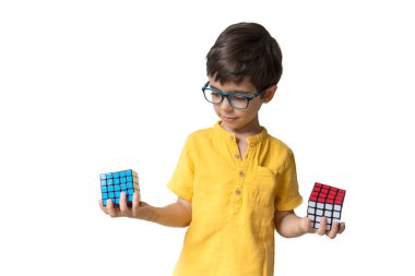 Gözlüklü entelektüel çocuk Rubik küpleriyle oynuyor. Beyaz arka planda izole edilmiş çocuk ellerinde Rubik küpü. Öğrenme kavramı.