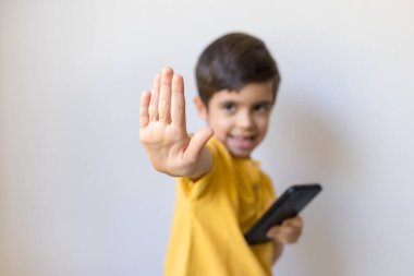 Cep telefonu olan sevimli küçük çocuk dur hareketi yap, kapat. Hayır de, kaprisler, duygular ve yüz ifadesi..
