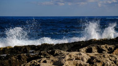 Mavi deniz dalgası, beyaz köpük ve su sıçraması. Malta adasında taş plaj, kumlu plaj yok. Yaz tatili sınır çerçevesi konsepti. Tropik ada tatili arka planı. Turist seyahat afişi tasarım şablonu.