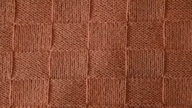 Örgü süveterin desenli bir görüntüsü. Üst manzara, yakın plan. El yapımı yün ya da pamuk kumaş dokusu. Alışılmadık soyut örülmüş satranç desenli arkaplan dokusu. 