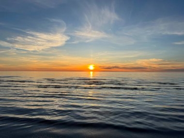 Okyanus dalgaları ve kıyıya karşı bulutlu turuncu günbatımı gökyüzü. Gündoğumu gökyüzü ile ilham verici sakin deniz. Suyun üstündeki renkli ufuk.. 
