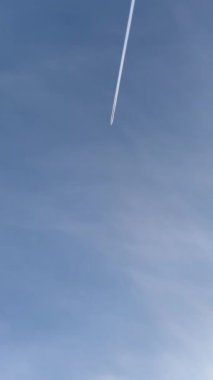 Mavi gökyüzünde uçarken parlak beyaz bir iz bırakan bir jet uçağı. Mavi gökyüzünde uçan bir uçağın manzarası. Grafikler ya da seyahat videoları için iyi bir arkaplan.
