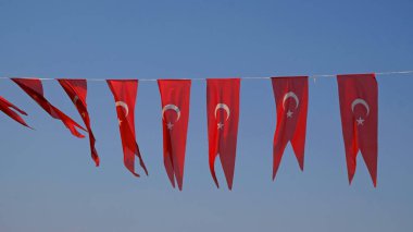 Birçok Türk bayrağı, ulusal bayram kutlamalarına hazır, mavi gökyüzüne karşı sallanıyor. Türk şehrinde sokak partisi dekorasyonu. Rüzgarda dalgalanan bayraklar.