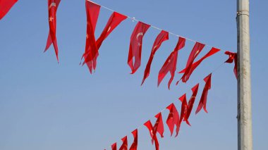 Birçok Türk bayrağı, ulusal bayram kutlamalarına hazır, mavi gökyüzüne karşı sallanıyor. Türk şehrinde sokak partisi dekorasyonu. Rüzgarda dalgalanan bayraklar.