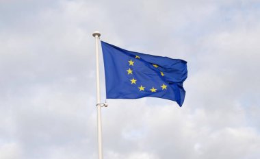 Avrupa Birliği bayrağı mavi gökyüzüne karşı bayrak direğinde rüzgarda sallanıyor. 12 sarı yıldızlı tek bir Avrupa bayrağına yakın çekim.