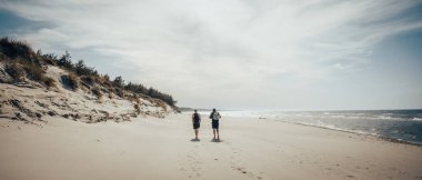 İki birey, engin okyanusun yakınındaki güzel kumlu bir sahilde etraflarındaki sakin atmosferin tadını çıkarıyorlar.