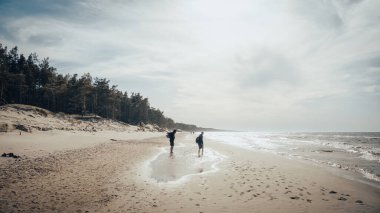İki birey, uçsuz bucaksız ve güzel okyanusun yanındaki kumlu bir plajda sakin bir şekilde yürümekten zevk alır.