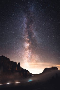 Sayısız yıldızla dolu çarpıcı bir gece gökyüzü bu güzel manzaranın ön planında duran görkemli bir dağı aydınlatıyor.