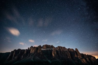 Sayısız yıldız gösteren güzel yıldızlı bir gece gökyüzü ve önde belirgin bir şekilde konumlanmış görkemli bir dağ.