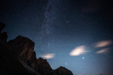 Sayısız yıldız gösteren güzel yıldızlı bir gece gökyüzü ve önde belirgin bir şekilde konumlanmış görkemli bir dağ.