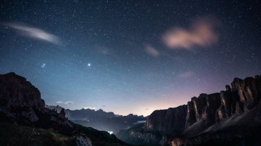 Parlayan yıldızlar ve görkemli dağlarla bezenmiş güzel yıldızlı bir gece göğü ön planda belirgin bir şekilde duruyor, nefes kesici bir manzara yaratıyor.