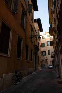 Kenarına park etmiş bir bisikletin olduğu dar bir cadde var. Binalar ve sakin bir atmosferle tuhaf bir manzara yaratıyor.