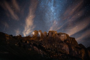 Sayısız yıldızla süslenmiş güzel bir gece gökyüzü ön planda beliren görkemli bir dağın üzerinde ışıldıyor.