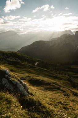 Güneş, uzak ufuktaki görkemli dağların üzerinde süzülen kabarık bulutların arasından ışıl ışıl parlıyor.