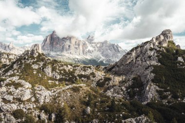 Uçsuz bucaksız gür ağaçlar ve engebeli kayalarla bezenmiş görkemli bir dağ bulutlu, dramatik bir gökyüzünün zeminine kurulmuş.