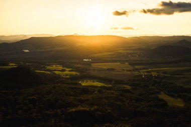 Sakin bir vadide nefes kesici bir gün batımı. Güneş akşam gökyüzündeki yumuşak bulutların arasından güzel bir şekilde parlıyor.
