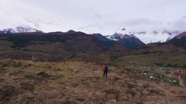 Sırt çantası ve Yürüyen Polonyalılarla Gezgin Hiker Adam Clouds ve El Chalten Town 'daki Fitz Roy Dağı' na bakıyor. Tepeler ve Dağlar. And Dağları, Patagonya, Arjantin. Hava görüntüsü. Yörüngede