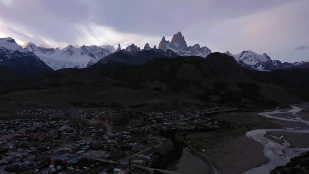 オレンジのバックパックを持つハイカー男立ち フィッツロイとセロトーレを見て チャルテン町 丘陵と雪に覆われた山々 アンデス パタゴニア アルゼンチン 空中展望 ドローンが後方に飛ぶ — ストック動画