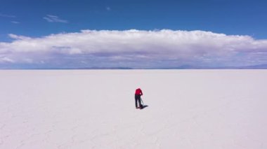 Tripod ve kameralı fotoğrafçı, güneşli bir günde Uyuni Tuz Düzlüklerine bakıyor. Hava görüntüsü. Altiplano, Bolivya. Kurak Mevsim. Tuz çatlakları ve oluşumları. Yörüngede. Solo Seyahat Konsepti