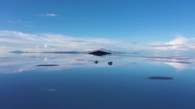 Uyuni Tuz Düzlükleri. Hava görüntüsü. Altiplano, Bolivya. Yağmur mevsimi. SUV arabaları, insanlar, Tunupa Volkanı ve Incahuasi Adası. Göl yüzeyinde Bulutların Yansıması. Drone İleri ve Yukarı Uçuyor